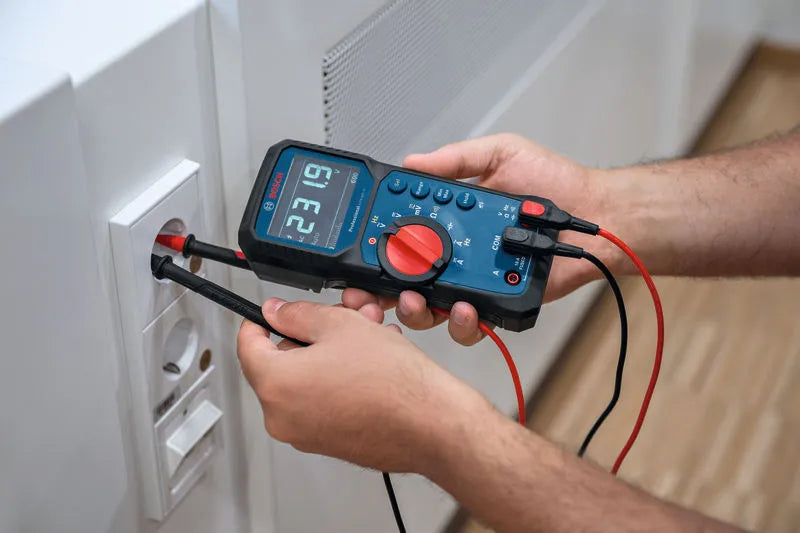 Person using a digital multimeter to check voltage on a wall socket.