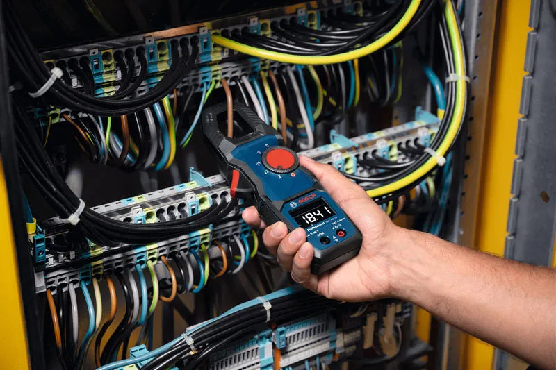 Person using a  clamp meter to check electrical connections in a panel with various cables.