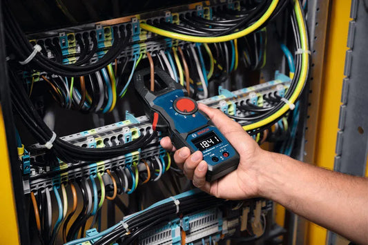Person using a clamp meter to check electrical connections in a panel with various cables.