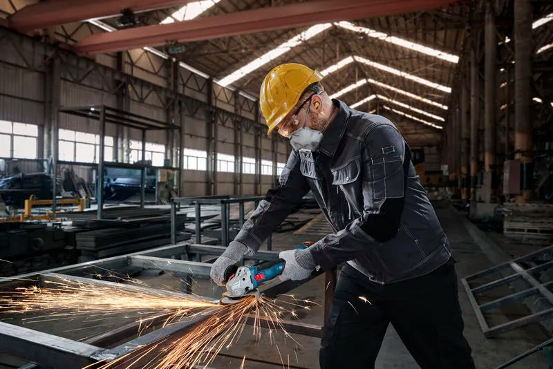 Worker using Bosch GWS 18V-8 cordless angle grinder with sparks in a warehouse setting
