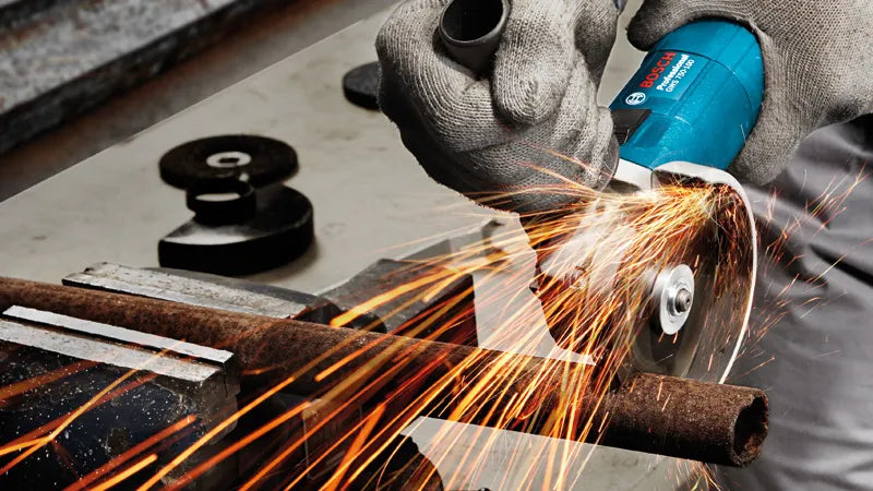 Person using a Bosch angle grinder GWS 750-115 on metal with sparks flying