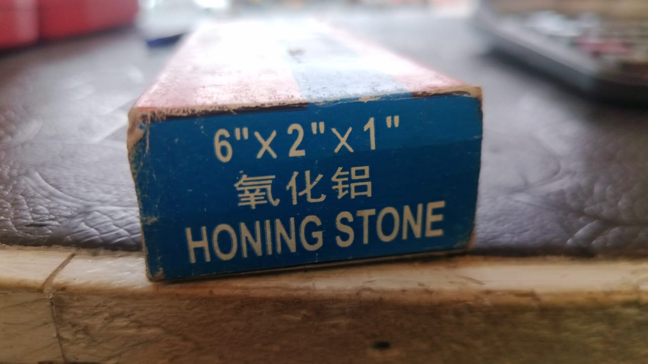 Honing stone with dimensions 6" x 2" x 1" on a blue label, placed on a textured surface.