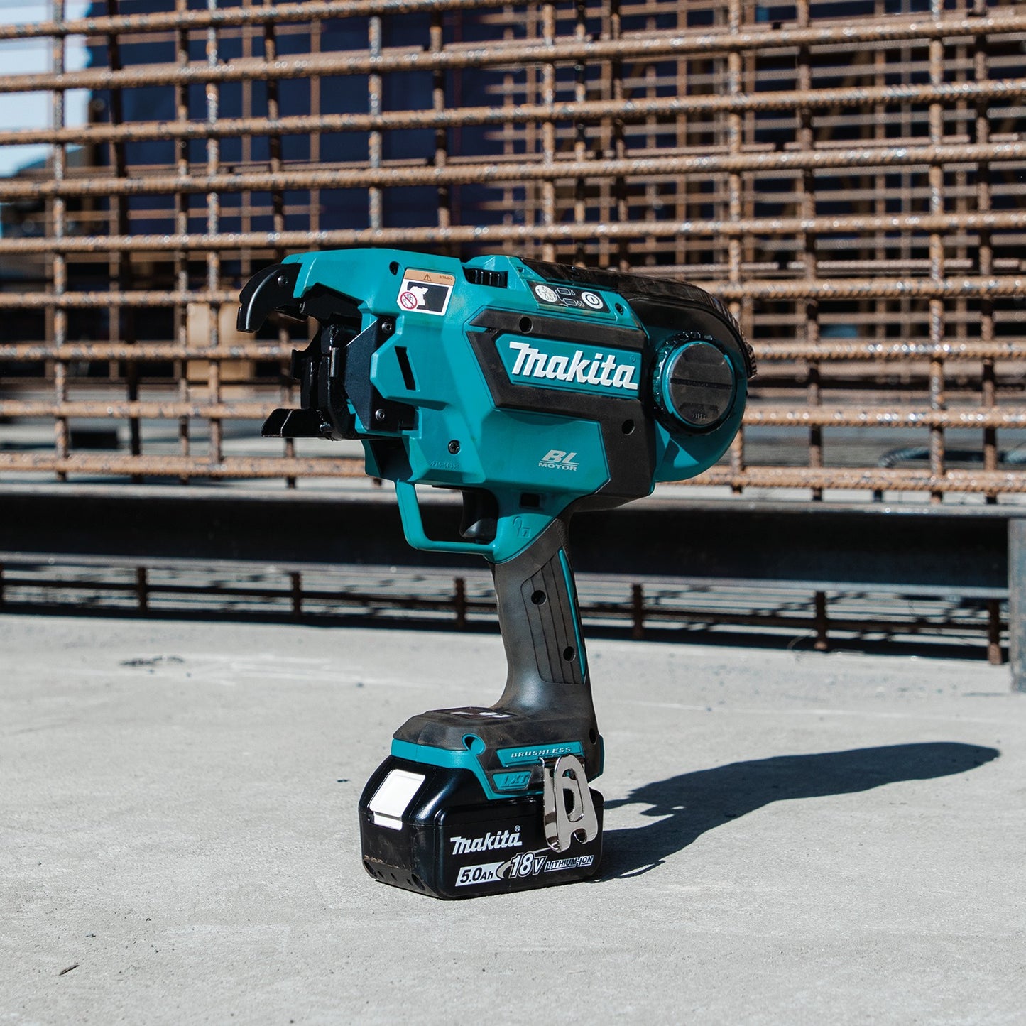 Makita cordless rebar tying tool on a concrete surface with a metal structure in the background